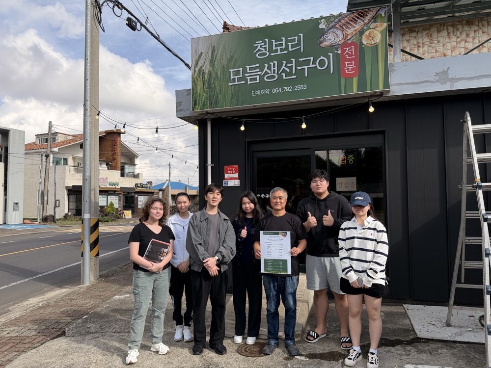 Owner of Cheongbori Assorted Grilled Fish holding the translated menu with the student team outside the restaurant