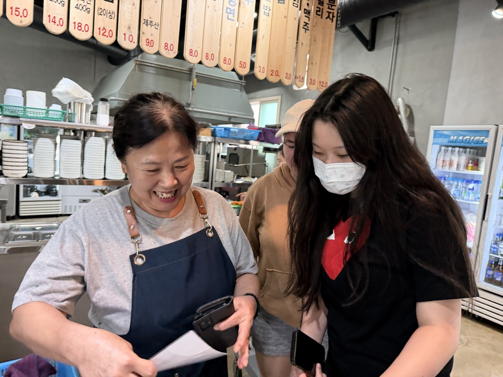 The owner of Donwarang laughing while reviewing a draft menu with a student
