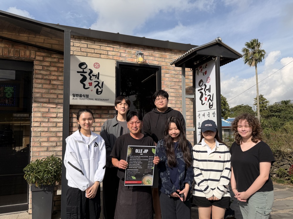 Owner of Olle Jip holding the new English menu in front of the brick restaurant with students