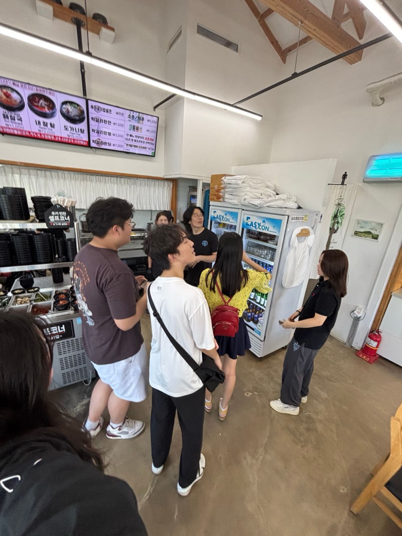 Students and staff standing at the counter of a haejangguk restaurant, looking at its menu screens
