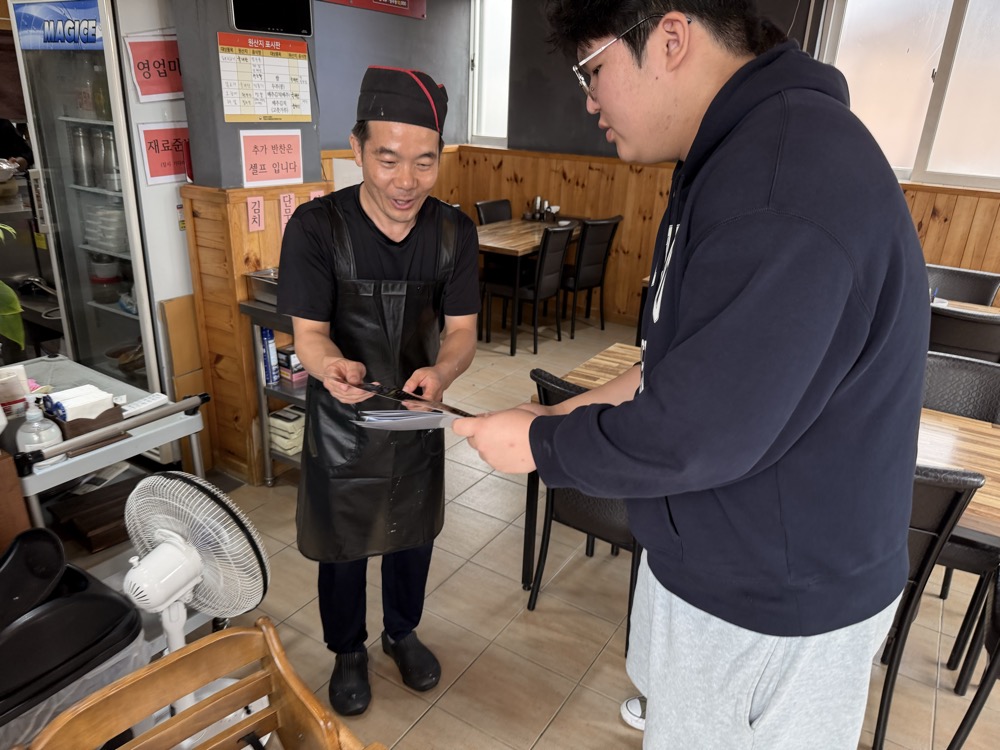 A student handing the finished menu to the owner of Soriwon inside the restaurant